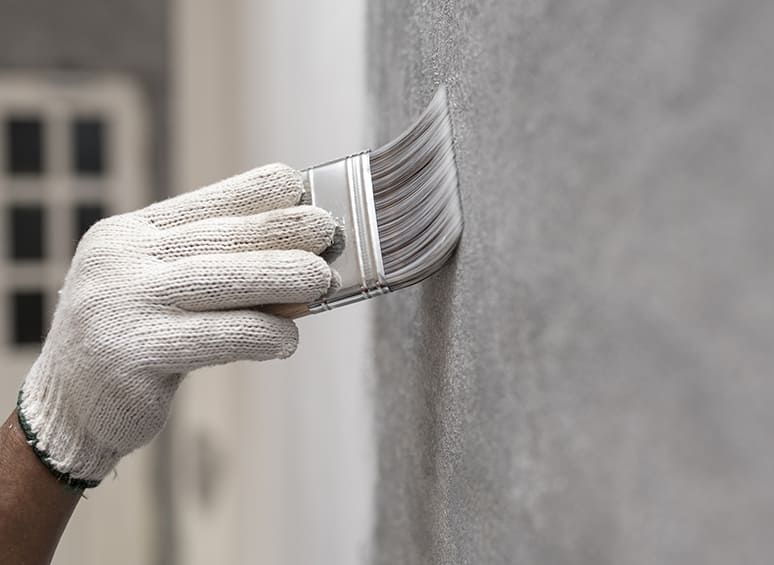 Hand mit einem Pinsel bestreicht die Wand mit einer transparenten Substanz