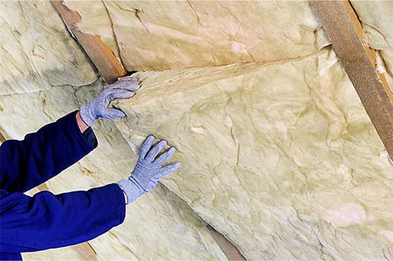 Person fügt Isoliermaterial für Wärmedämmung in eine offene Wand