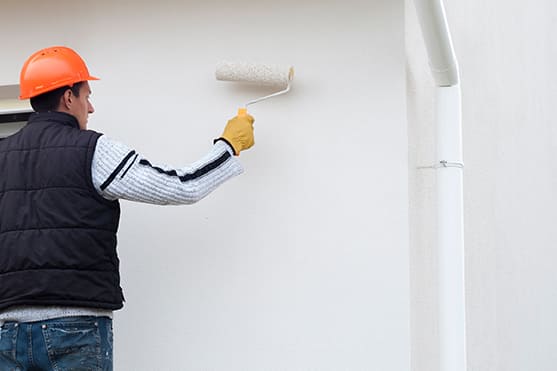 Maler trägt einen Helm und Handschule und streicht eine Wand mit weißer Farbe